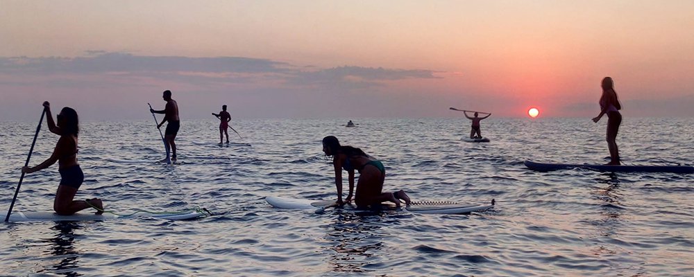 people on sup boards at sunset